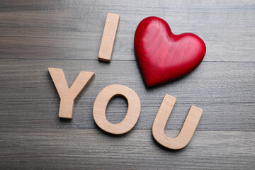 Phrase I Love You made of decorative heart and letters on wooden background, above view