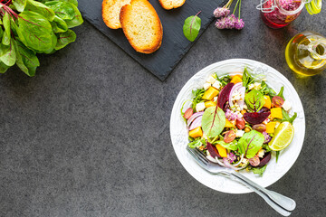 Fresh vegetable salad with beets, arugula, red onions, sorrel, chickpeas, pumpkin in a white plate on a black background. Top view