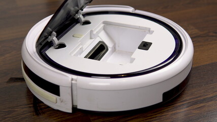 Fototapeta premium A dirty filter is pulled out of a vacuum cleaner robot. Automatic white round vacuum cleaner
