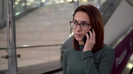 A young woman rides on an escalator and speaks on the phone. Large shopping center