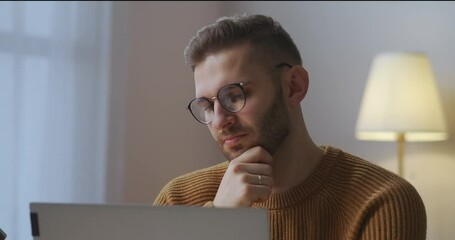 boring man with glasses is listening and looking at screen during online meeting with colleagues, sitting at home, nodding head