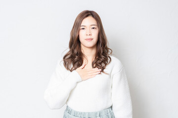 Fototapeta premium 白い壁の前に立って胸に手を当てる若い女性