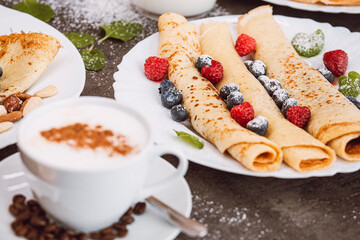 Cup of cappuccino coffee with coffee beans. In the background served pancakes with fruit