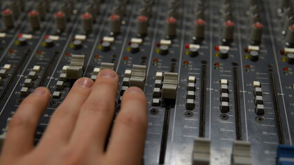 The man adjusts the sound using the sliders on the panel. Mixer for controlling and adjusting sound. Old specialized professional equipment.