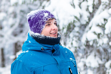 Portrait of happy handsome guy in a winter snowy forest. Young man playing, enjoying walking outdoors in warm clothers in snow, smiling. Snowball game.