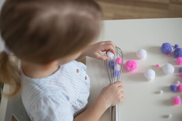 Toddler fine motor and learning activity with household items. DIY, child pulling out whisk with pom pom. - obrazy, fototapety, plakaty