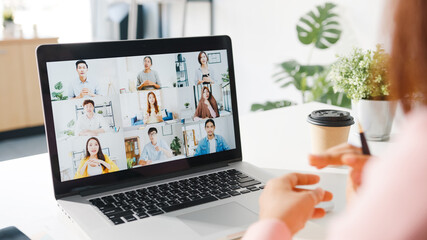 Young Asia businesswoman using laptop talk to colleague about plan in video call meeting while work from home at living room. Self-isolation, social distancing, quarantine for corona virus prevention.