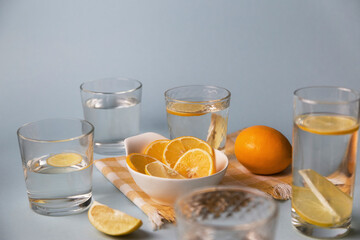 Many glasses with water and lemon slices for drinking stands on a blue background, in the middle of a white bowl with lemons
