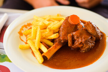 Portion of goat meat in red sauce with french fries served on a plate, restaurant background