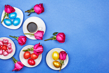 Easter eggs, red rose flowers, a cup of black coffee on blue background