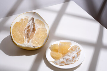 Fresh pomelo half, wedges and pulp on white background in sunlight.
