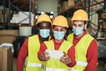 Happy multiracial workers taking a selfie inside warehouse while waring safety masks - Delivery and...