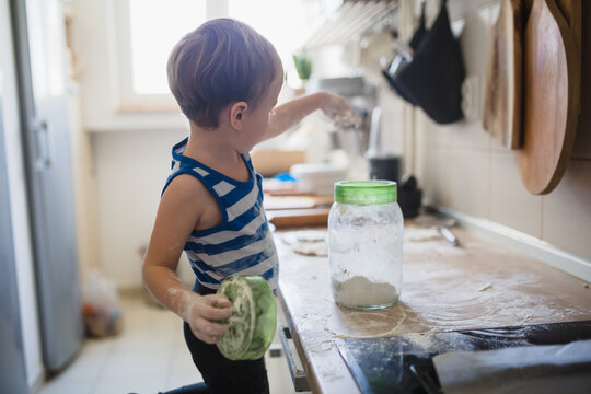 cute little boy playing with flour and making mess in kitchen