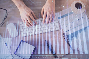 Multi exposure of man's hands typing over computer keyboard and forex graph hologram drawing. Top...