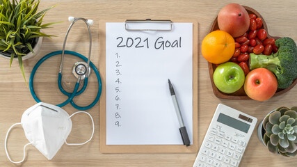 2021 New Year Goals in new normal lifestyle, work-life balance with face mask safety from covid-19, healthy  cholesterol diet food, good heart health on blank resolution list on paper medical notepad