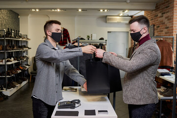 A man in a face mask to avoid the spread of coronavirus is taking his purchase from a seller in a...