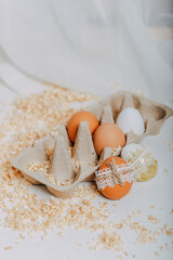 Easter eggs in carton box on white background with sawdust around. Easter eggs with lace border around. Process of decorating easter eggs with lace and rope. Golden easter egg with glitters.