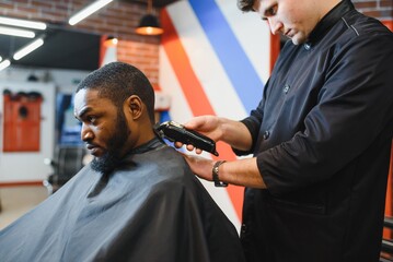 Portrait of young black man being trimmed with professional electric clipper machine in...