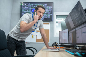 Man near monitors talking on smartphone