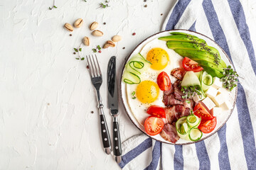 Healthy nutritious paleo keto breakfast with egg, bacon, avocado, cheese and fresh salad on white plate on light background. Flat lay
