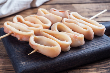 Fried squid rings on a skewer with tomato sauce and lemon. Dark wooden background copy space. Top...