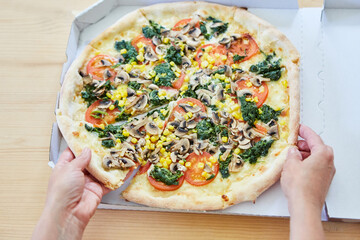 Hand while dividing vegetable pizza with pizza slice