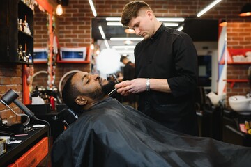 Side view of serious man with stylish modern haircut looking forward in barber shop. Hand of barber keeping straight razor and cutting trendy stripes on head of client.