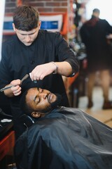 Side view of serious man with stylish modern haircut looking forward in barber shop. Hand of barber...