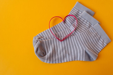 Red heart on gray socks with white stripes on a yellow background, top view, space for text