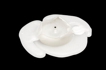 A burnt white, thick candle with molten paraffin wax on black bckground. Close-up blurred in soft...