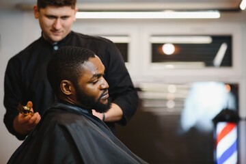 Portrait of young black man being trimmed with professional electric clipper machine in...