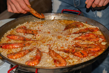 The chef prepares a paella with seafood and vegetables. He puts the prawns on the rice.