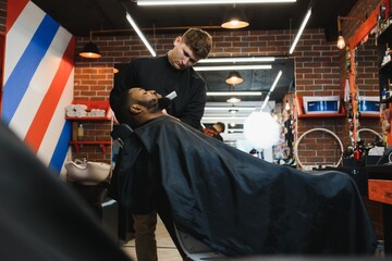 Closeup of process of trimming of hair in barber shop. Qualified barber keeping clipper in hands and correcting shape of hair to male client sitting on chair. Concept of haircut and shaving.