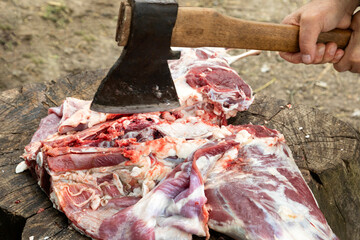 Butchering meat with an ax on a stump. A hand with an ax cuts the meat into pieces for further cooking. Natural food.