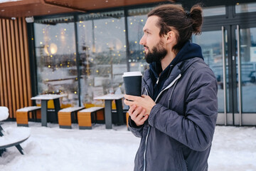 Portrait of cheerful attractive bearded driver enjoying hot coffee, looking by side outdoors near a...