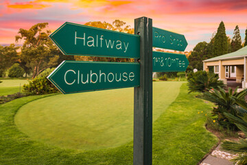Golf course direction signs on fairway and colorful sunset