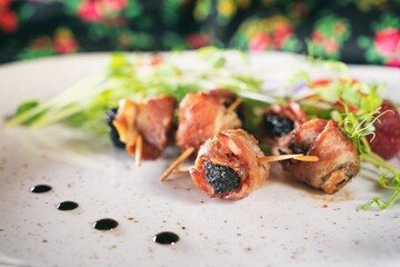 Plum in crispy bacon on a plante. Dinner appetizer on a wooden table. Traditional polish cuisine