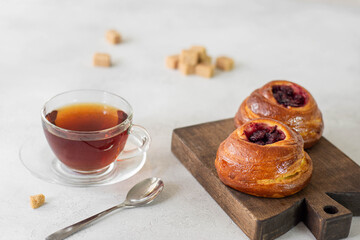 Sweet buns with cherries on a wooden board. Nearby a cup of tea in a glass cup