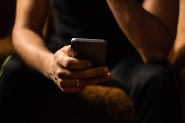 Close up of a man sitting in a chair at home with a mobile phone in his hand with a blurred background