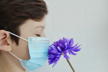 A masked boy sniffs a flower.