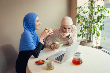 Sincere. Beautiful arab women meeting at cafe or restaurant, friends or business meeting. Spending time together, talking, laughting. Muslim lifestyle. Stylish and happy models with make up.