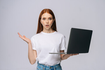 Surprised displeased young woman student holding keeping opened laptop computer and looking at...