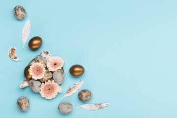 Easter Decoration with gray golden eggs, quail feathers, flowers on blue background. Happy Easter card concept, top view.