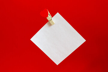white sheet for notes on a red background with a clothespin with a heart on a whip rope for inscriptions