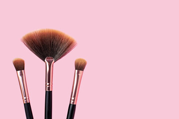 A set of professional makeup brushes on a pink background. Stylish makeup artist tools in black and rose gold color. Concept for womens cosmetics, beauty concept, skincare. Copy space.