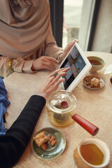 Close up scrolling tablet. Beautiful arab women meeting at cafe or restaurant, friends or business meeting. Spending time together, talking. Muslim lifestyle. Stylish and happy models with make up.