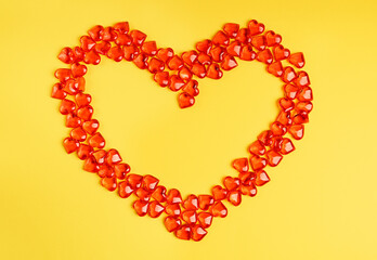 Obraz premium Small red heart shape transparent candies or glass decorations laying on bright vibrant yellow background as a lovely greeting card on saint valentine's day. Image with copy space, horizontal