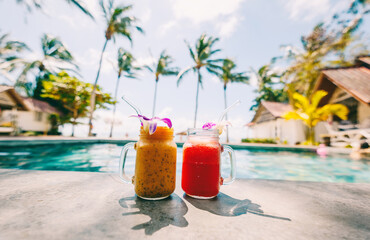Fruit cocktails in glasses decorated with orchids by the pool overlooking the tropical sea and palm trees