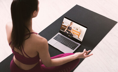 Young woman meditating or doing yoga, following online video instructions from personal trainer, above view