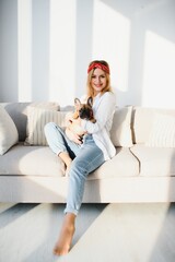 Cheerful young woman holding her big puppy with black nose and laughing. Indoor portrait of smiling girl posing with french bulldog